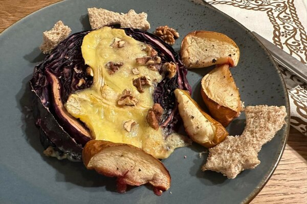 Eine Scheibe Rotkohl mit Käse überbacken, dazu Nüsse, Apfel- und Birnenspalten auf einem Teller.