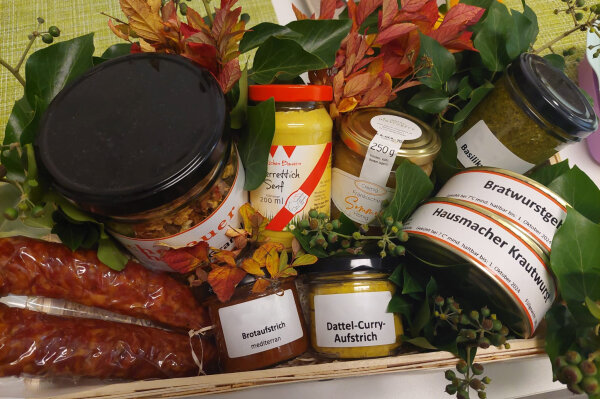 Geschenkkorb mit Senfglas, Brotaufstrichen, Dosenwurst, grünem Pesto, geräucherten Bratwürsten und Honig
