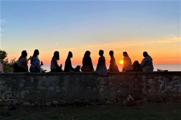 Emma und acht ihrer Klassenkameradinnen betrachten auf einer Mauer gemeinsam den Sonnenuntergang