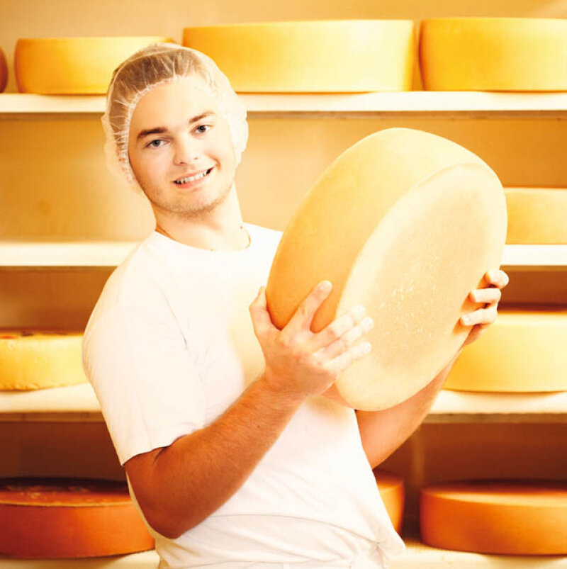 Ein junger Mann mit Haarnetz hält einen Laib Käse hoch
