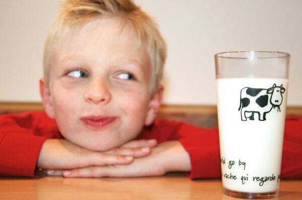 Kind hat Kopf auf Hände gelegt und schielt auf Glas mit Milch