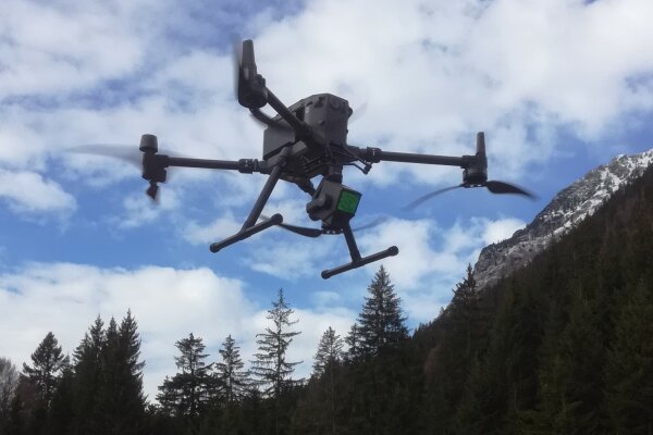 Fliegende Drohne vor einer bewaldeten Bergkulisse