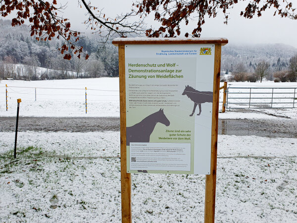 Informationsschild vor einer Zaunanlage in verschneiter Landschaft