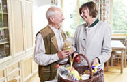 Eine Fachhauswirtschafterin steht mit einem älteren Herren vor einem Korb mit Einkäufen