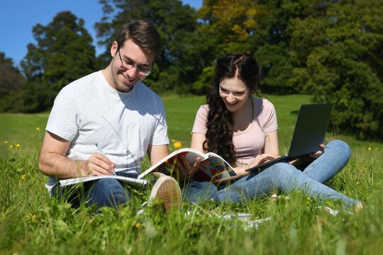 Ein junger Mann und eine junge Frau sitzen gemeinsam im Gras und lernen.