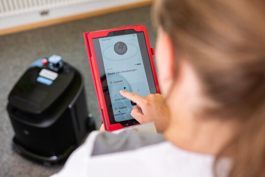 Hauswirtschaftliche Fachkraft bedient einen Reinigungsroboter mit einem Tablet.