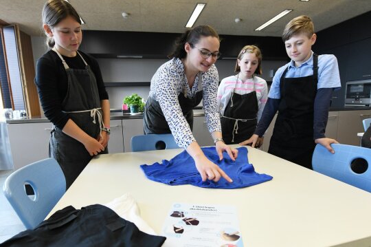 Lehrerin zeigt Gruppe von Schülern wie man T-Shirts faltet.