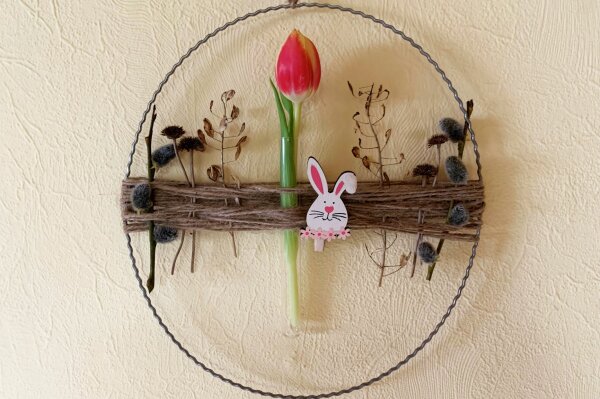 Ein Metallkranz mit Trockenblumen, einer Häschenklammer und einer Tulpe in der Mitte.