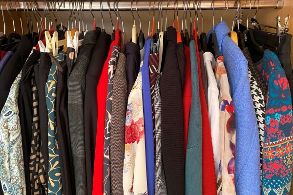 Verschiedene Blusen und Sakkos hängen in einem Kleiderschrank an Bügeln.