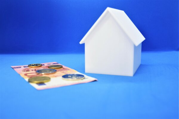 Modell eines Hauses, daneben liegen Geldscheine.