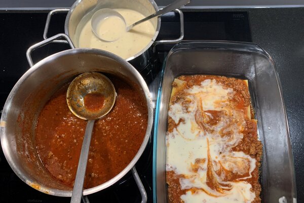 Zwei Töpfe mit einer Bechamel- und einer Bolognese-Sauce stehen neben einer Aufllaufform.