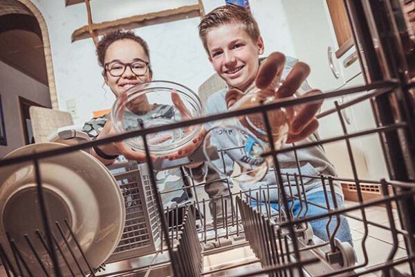 Zwei Kinder räumen Geschirr in eine Geschirrspülmaschine