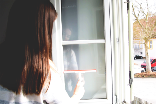 Junge Frau reinigt Fenster mit einem Abzieher.