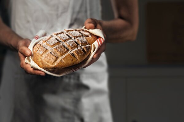 Bäcker hält einen Laib Brot in der Hand.