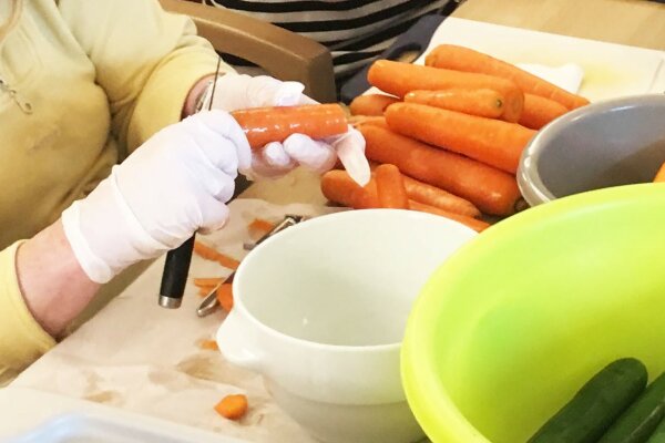 Nahaufnahme einer behandschuhten Hand, die Karotten schält.