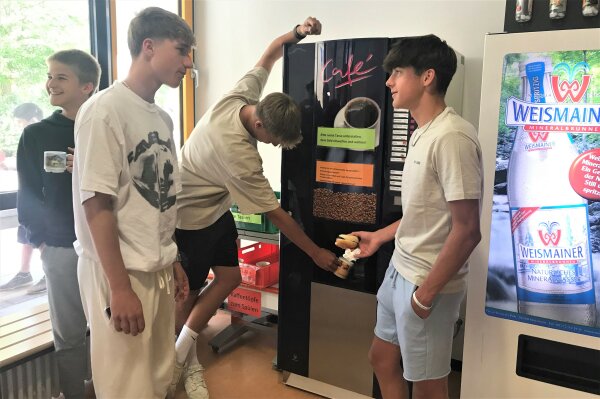 Schüler stehen vor einem Kaffeeautomaten in einer Schulkantine.