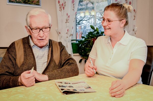 Senior und Pflegerin unterhalten sich gemeinsam am Tisch sitzend