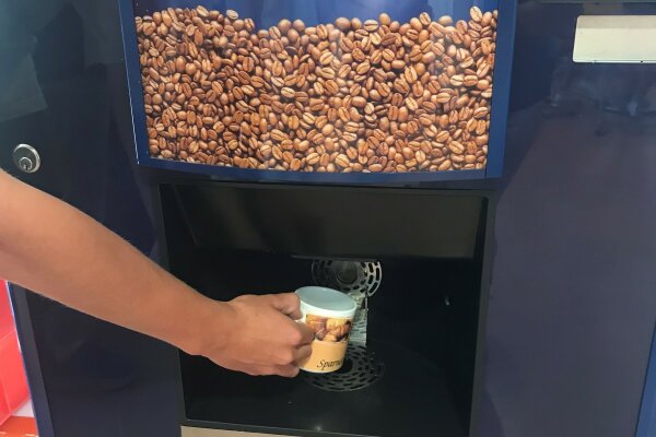 Eine Hand hält eine Porzeallantasse unter einen Kaffeeautomaten.