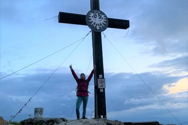 Annika vor einem Gipfelkreuz in den Bergen