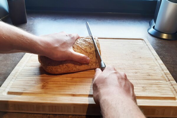 Person schneidet Brot auf einem Holzbrett