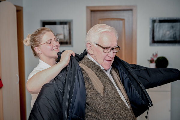 Pflegerin hilft Senior in die Jacke