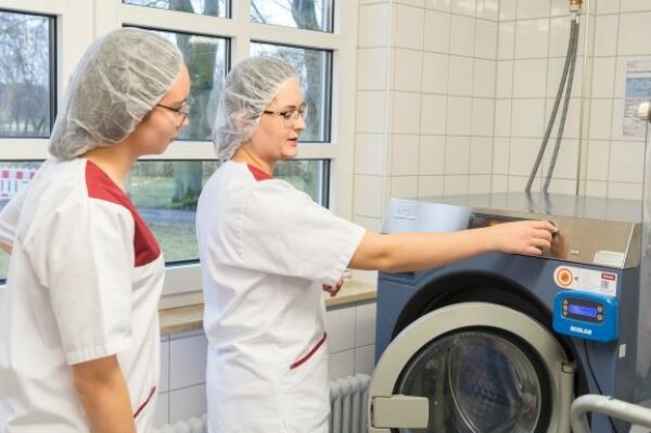 Zwei junge Frauen stehen an einer industriellen Waschmaschine.