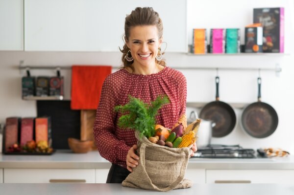Junge Frau mit einer Tasche voller Obst und Gemüse in der Küche.