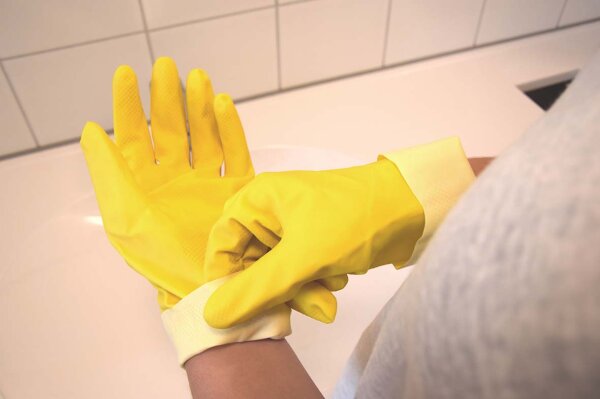 Person zieht sich Reinigungshandschuhe über.