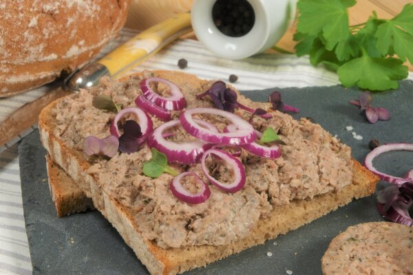 Brotzeitplatte mit Leberwurstbrot garniert mit roten Zwiebeln und einem Laib Brot.