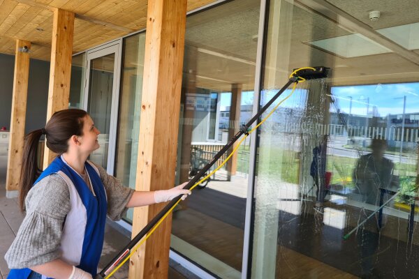 Marie reinigt ein Fenster mit einem professionellen Reinigungsgerät.