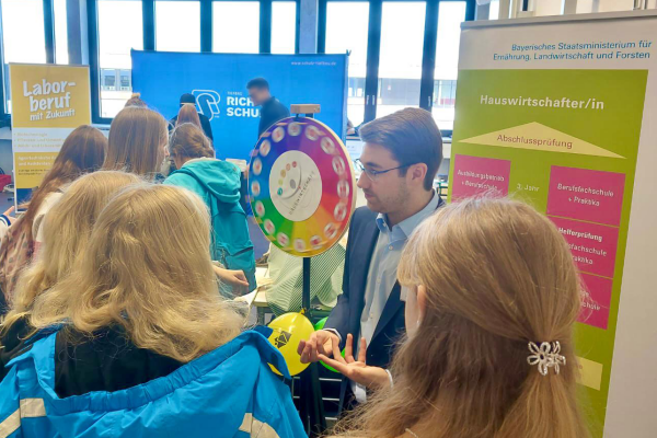 Mehrere junge Leute versammeln sich vor einem Glücksrad auf der Messe.