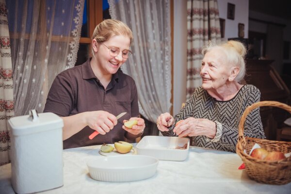 Pflegerin schneidet Äpfel mit Seniorin