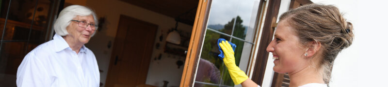 Dienstleisterin reinigt Fenster bei einer Seniorin