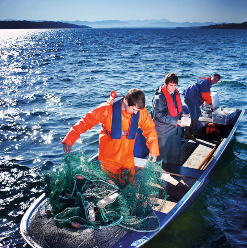 ein junger Mann in orangefarbenem Schutzoverall mit Fischernetzen auf einem kleinen Fischerboot