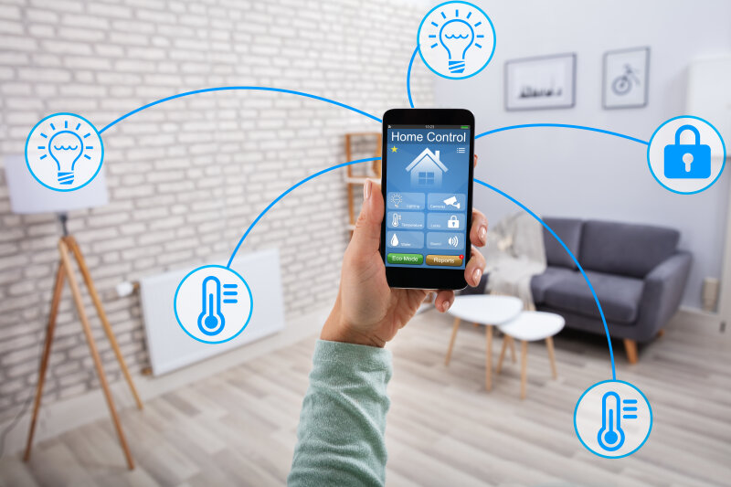Person hält ein Smartphone in ein Wohnzimmer, außenrum blaue Icons zum Thema Smart Home