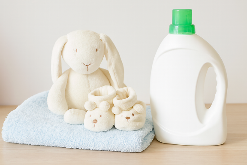 Ein Stofftier und Babyschuhe stehen auf einem Handtuch. Daneben steht eine Waschmittel-Flasche. 