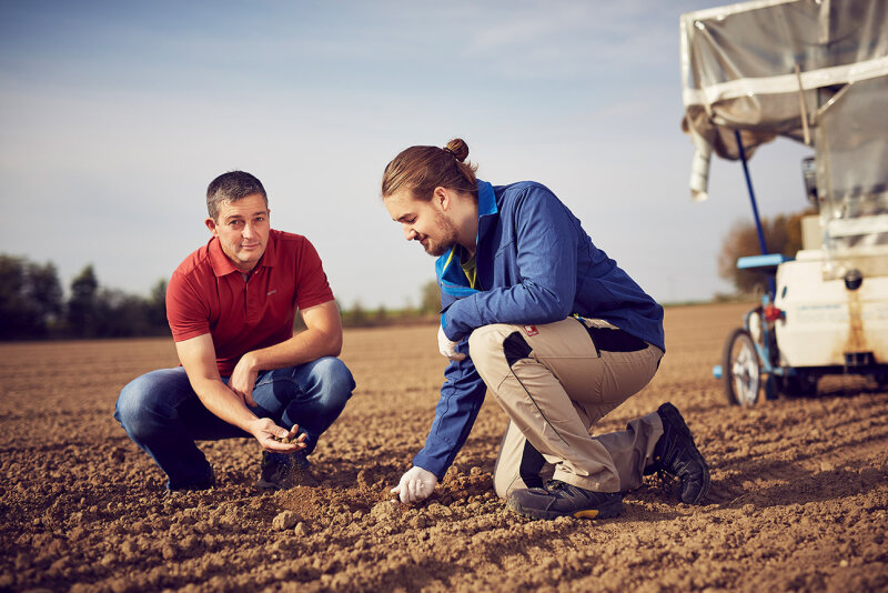 zwei Männer knien neben einer Maschine auf einem Acker und untersuchen den Boden