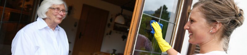 Fachkraft reinige Fenster und unterhält sich mit Seniorin
