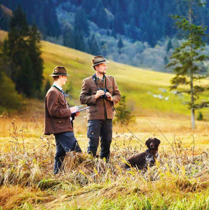 zwei Männer mit Hut und ein Hund stehen in einer Wiese