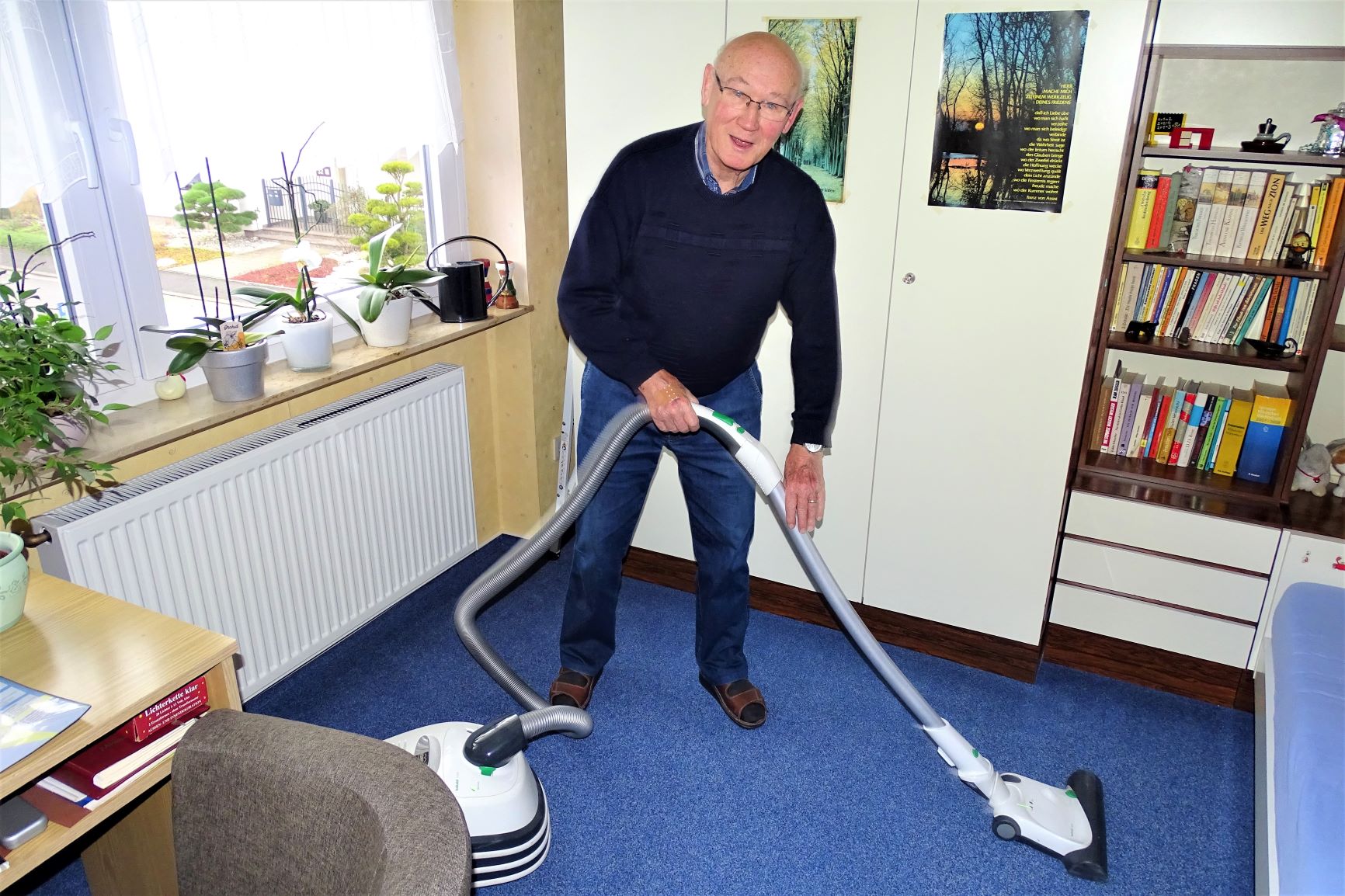 Ein Senior staubsaugt ein Zimmer