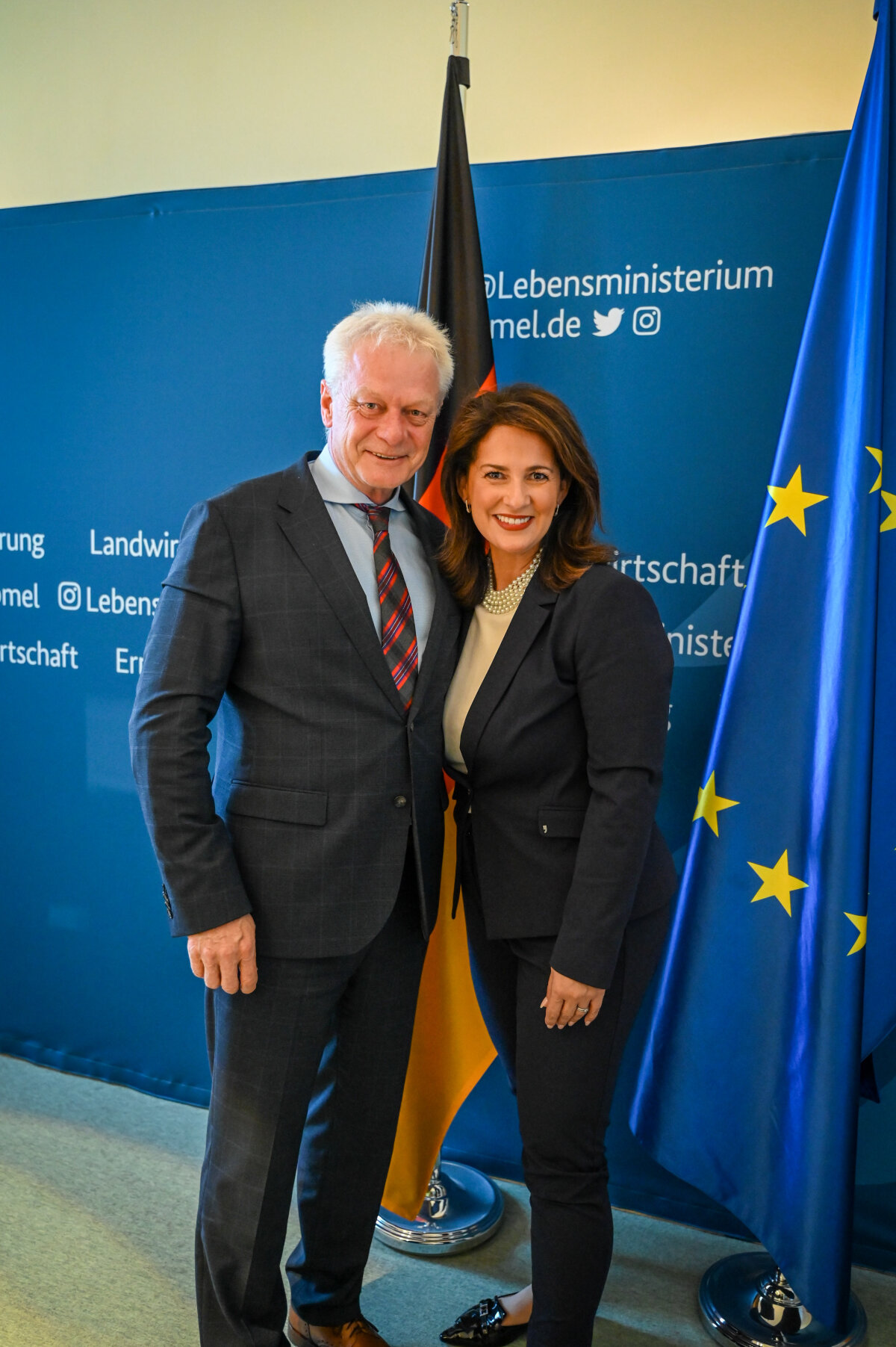 Das Bild zeigt Staatsministerin Kaniber zusammen mit Bundesminister Rainer vor einer blauen Bannerwand sowie einen Deutschland- und Europafahne.