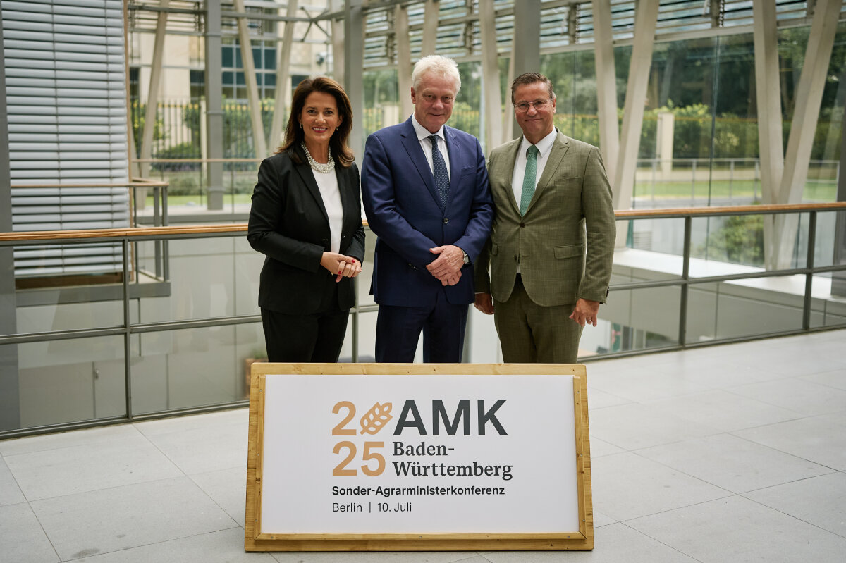 Das Bild zeigt Staatsministerin Kaniber zusammen mit Bundesminister Alois Rainer und dem Vorsitzenden der Agrarministerkonferenz, Baden-Württembergs Landwirtschaftsminister Peter Hauk hinter einem Holzschild auf dem steht: AMK 2025 Baden-Württemberg.