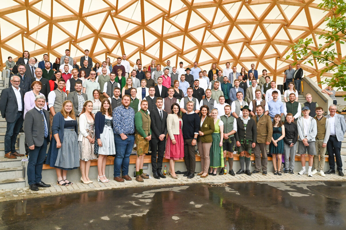 Das Bild zeigt Ministerin Michaela Kaniber zusammen mit einer großen Gruppe neuer Gärtnermeisterinnen und Gärtnermeister vor einer Holzkuppel, viele in Tracht oder festlicher Kleidung.