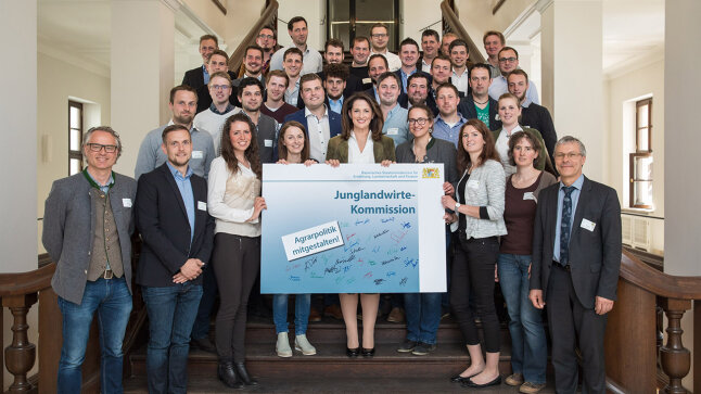 Eine Gruppe von Personen auf einer Treppe. Im Vordergrund die Ministerin mit einem großen Schild mit Unterschriften und den Worten "Junglandwirte-Kommisssion. Agrarpolitik mitgestalten!"