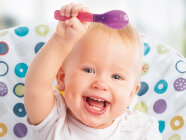 Ein lachendes Baby hält einen Löffel hoch