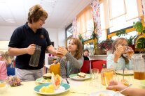 Frau reicht einem Schulkind beim Mittagessen ein Getränk