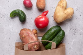 Eine Papiertüte und Gemüse: Gurken, Karotte, Radieschen, Kartoffel, Tomate