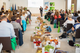 Menschen in einem Veranstaltungssaal, in der Mitte stehen Kartons mit Lebensmitteln