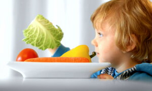 Kind sitzt vor einem Teller mit Gemüse und hält Wirsingblatt in der Hand