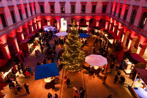 Blick in den rot beleuchteten Innenhof des Landwirtschaftsministeriums mit Ständen zum Hoffest und Besuchern.